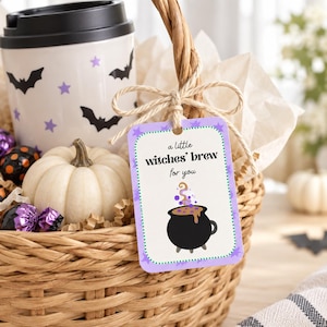 May include: A woven wicker basket containing a white travel mug with black bats and purple stars, a small white pumpkin, and purple wrapped candies. A rectangular tag tied with twine reads, a little witches' brew for you, with a black cauldron graphic.