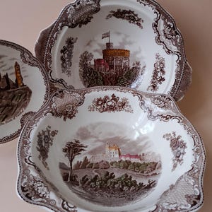 以下が含まれることがあります： 白と茶色のアンティーク装飾ボウル3つ。縁はスカラップ模様。各ボウルの中央には異なる風景画があり、花柄とスクロール模様のボーダーが付いています。ボウルはおそらく陶器または磁器製です。
