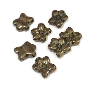 Könnte beinhalten: Eine Sammlung von sieben metallisch goldenen, blüten- und sternförmigen Perlen. Die Perlen haben eine glänzende, leicht strukturierte Oberfläche.