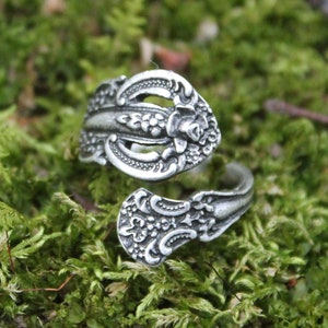 May include: A silver ring made from a vintage spoon, with intricate floral designs. The ring is shown on a bed of green moss.
