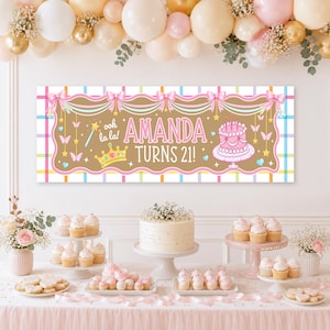 May include: A rectangular party banner featuring a tan center with a pink border, white bows, and a plaid frame. The text reads AMANDA TURNS 21! with a pink cake, a gold crown, and a magic wand graphic. The banner is displayed above a dessert table.