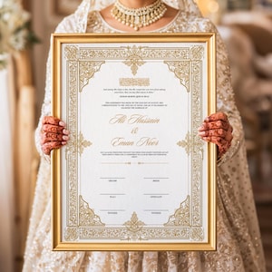 May include: A framed wedding certificate with gold ornate borders and text. The certificate is held by a person wearing a white dress and jewelry. The names "Ali Hussain & Eman Noor" are visible.