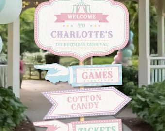 Könnte beinhalten: Ein Satz Schilder im Karneval-Stil für eine Geburtstagsfeier. Das Hauptschild lautet "WELCOME TO CHARLOTTE'S 1ST BIRTHAY CARNIVAL". Weitere Schilder weisen auf "SPIELE", "ZUCKERWATTE" und "TICKETS" hin. Die Schilder sind pastellrosa, blau und weiß.