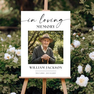 Könnte beinhalten: Ein weißes Gedenkschild mit dem Text "in loving MEMORY" oben, einem zentralen Foto einer älteren Person mit Strohhut und dunklem Pullover sowie dem Namen "WILLIAM JACKSON" mit den Daten "MAY 5, 1960 - OCT 15, 2025".