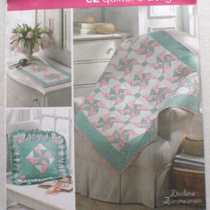 Op de afbeelding: Simplicity ez quilter's delight patroon. De afbeelding toont een quilt, een kussen en een tafelloper met een roze en blauwgroen geometrisch ontwerp. Het patroon bevat de tekst "3703" en "ONE SIZE".