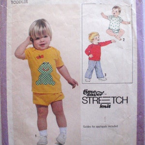 Pode incluir: Um padrão de costura para um conjunto de criança pequena. O padrão inclui instruções para uma camisa amarela com uma aplicação de sapo, um short amarelo e uma camisa vermelha com calças listradas. O padrão é para os tamanhos 1/2, 1 e 2. O padrão é chamado de "Time Saver Stretch Knit".