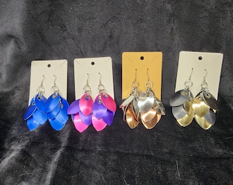 May include: Four pairs of dangle earrings with five layered metal leaves. The earrings are displayed on white and brown card stock. The leaves are in blue, pink, silver, and gold.