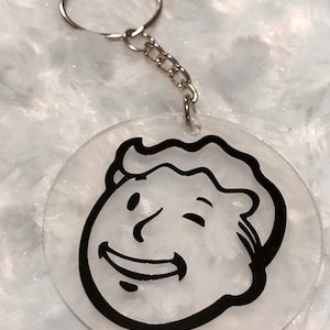 May include: A clear, circular keyring featuring a black and white cartoon face with a smiling expression. The keyring has a silver chain and key ring attached. The design is a popular video game character.