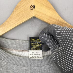 May include: A gray sweatshirt with a crew neck, hanging on a wooden hanger. The tag reads "BODY GLOVE" and "MADE IN JAPAN". The sweatshirt is size medium.