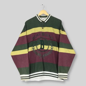 May include: A long-sleeved striped shirt in green, yellow, and burgundy, with a white collar and cuffs. The shirt has the text "BDG" with a "B" in a laurel wreath. The shirt is hanging on a wooden hanger.
