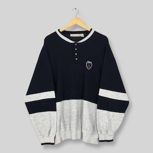 May include: A navy blue and gray long-sleeve sweatshirt with a button-up collar and a small emblem on the chest. The sweatshirt has white stripes on the sleeves and a gray bottom half. The collar and cuffs are trimmed in white.