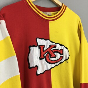 May include: A red and yellow sweatshirt with the Kansas City Chiefs logo. The sweatshirt is split vertically, with red on the left and yellow on the right. The logo is white with red and black accents.