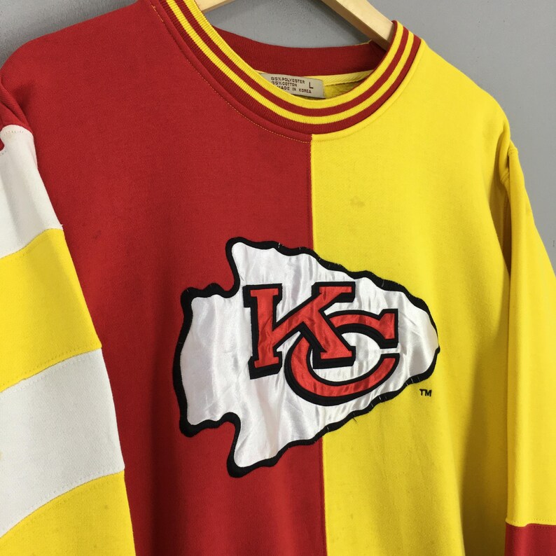 May include: A red and yellow sweatshirt with the Kansas City Chiefs logo. The sweatshirt is split vertically, with red on the left and yellow on the right. The logo is white with red and black accents.