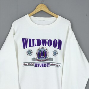 May include: White sweatshirt with the word "WILDWOOD" in purple block letters. Below the word is a graphic of sailboats and the text "WORLD REGATTA". The text "NEW JERSEY" is also visible.