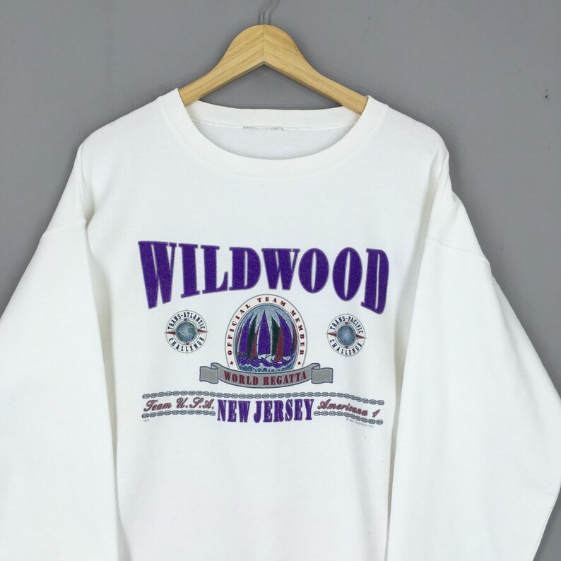 May include: White sweatshirt with the word "WILDWOOD" in purple block letters. Below the word is a graphic of sailboats and the text "WORLD REGATTA". The text "NEW JERSEY" is also visible.
