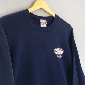 May include: A navy blue sweatshirt featuring the Ron Jon Surf Shop logo in white and red. The sweatshirt is displayed on a wooden hanger. The logo is on the chest.