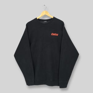 May include: Black crew neck sweatshirt with the red "Castrol" logo on the chest. The sweatshirt is hanging on a wooden hanger. The garment has long sleeves and a ribbed neckline, cuffs, and hem.