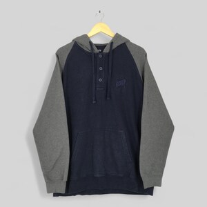 May include: A navy blue and gray hoodie with a hood and long sleeves. The hoodie has a button-up neckline and a kangaroo pocket. A small emblem is embroidered on the chest.