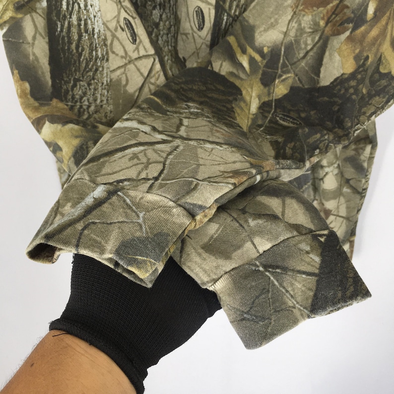 Peut inclure: Chemise &agrave; manches longues camouflage avec un motif forestier dans les tons marron, vert et beige. Le tissu est visible sur les manches et les poignets. La chemise est faite d'une mati&egrave;re douce et confortable.