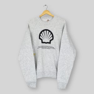 Könnte beinhalten: Ein hellgraues Sweatshirt mit einem schwarzen Muschellogo und Text. Das Sweatshirt hängt an einem Holzkleiderbügel. Der Text lautet: "with our superior technology and knowledge...for your total satisfaction."