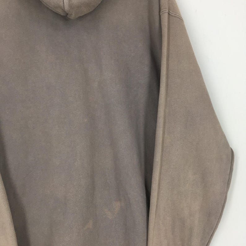 Puede incluir: Una sudadera con capucha de color marr&oacute;n claro con capucha y mangas largas. La tela tiene un aspecto ligeramente descolorido, con sutiles variaciones de color y textura. La sudadera con capucha est&aacute; hecha de un material suave.