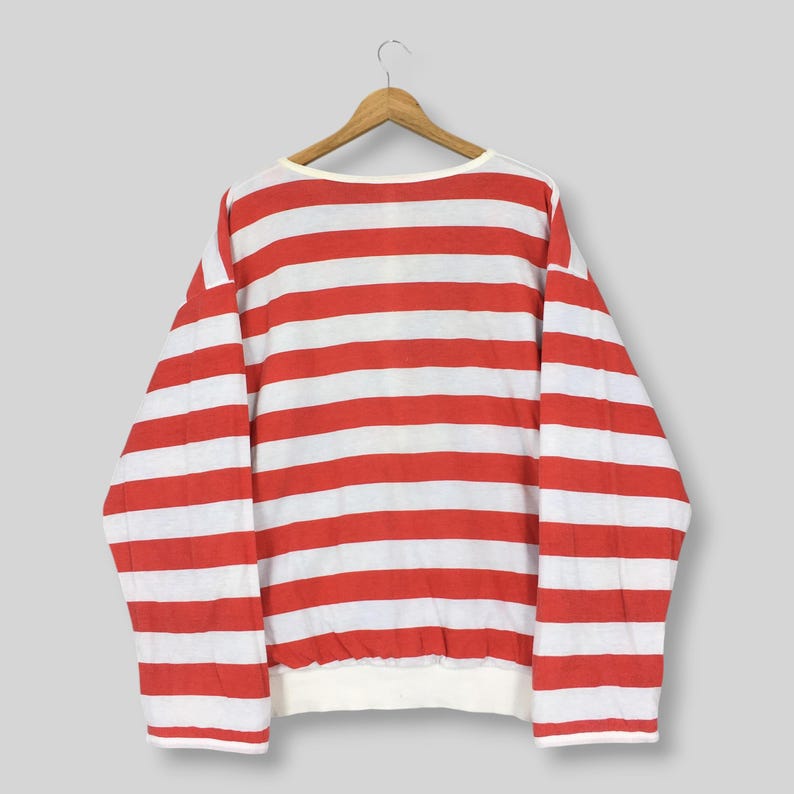 May include: A long-sleeve pullover sweatshirt featuring a horizontal striped pattern in vibrant red and white. The garment has a wide crew neckline, long sleeves, and a ribbed hemline, displayed on a wooden hanger against a neutral background.