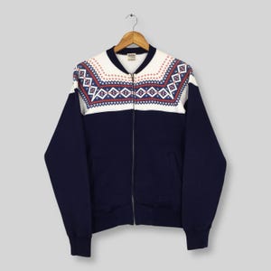 May include: A vintage navy blue zip-up jacket with a white yoke featuring a geometric pattern in red and blue. The jacket has a ribbed collar, cuffs, and hem, and two front pockets. The jacket is hanging on a wooden hanger.
