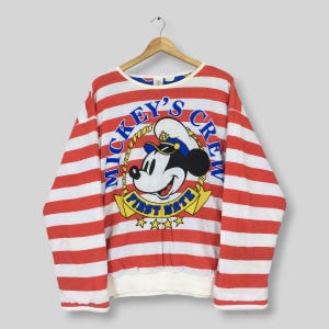 May include: A long-sleeve sweatshirt featuring horizontal red and white stripes. The center graphic displays Mickey Mouse wearing a sailor hat, surrounded by the text Mickey's Crew and First Mate, with a yellow rope border and four yellow stars.