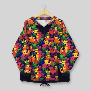 May include: A long-sleeved pullover with a vibrant pattern of colorful koala bears. The top features a navy blue collar, zipper, and drawstring hem. The koalas are in shades of yellow, green, orange, and purple against a dark blue background.
