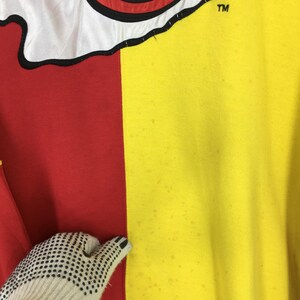 May include: A close-up of a two-toned garment, with a red and yellow color block design. The top portion features a white section with a black outline. The upper right corner has the letters "TM".