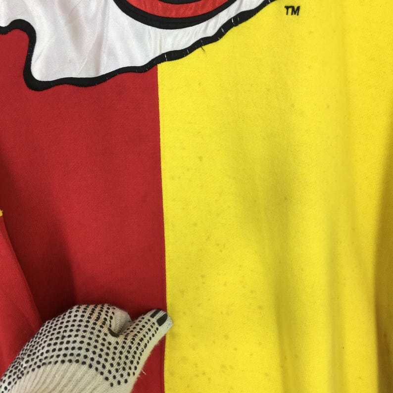 May include: A close-up of a two-toned garment, with a red and yellow color block design. The top portion features a white section with a black outline. The upper right corner has the letters "TM".
