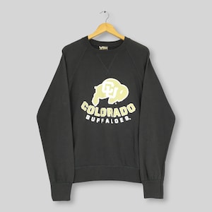 May include: A charcoal gray long-sleeve sweatshirt featuring a cream-colored graphic of a buffalo silhouette and the text "COLORADO BUFFALOES" with a "CU" logo on the chest. The garment has a crew neckline and ribbed cuffs and hem.