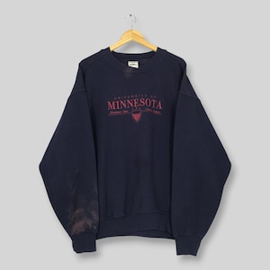 Puede incluir: Sudadera azul marino con el texto rojo "UNIVERSITY OF MINNESOTA" en el pecho. El texto incluye el año "Established 1851". La sudadera tiene cuello redondo y mangas largas.