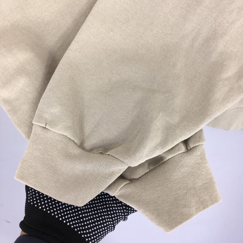 K&ouml;nnte beinhalten: Nahaufnahme eines beigefarbenen Langarm-Shirt-&Auml;rmels. Das B&uuml;ndchen ist gerippt und der Stoff scheint eine weiche Baumwollmischung zu sein. Der &Auml;rmel ist leicht zerknittert.