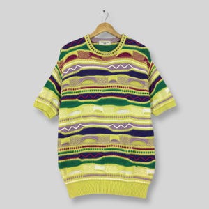 May include: A short-sleeved, multi-colored knit sweater with a vibrant, geometric pattern. The sweater features horizontal stripes in shades of yellow, green, purple, and red. The garment is hanging on a wooden hanger against a neutral background.