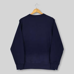 May include: A solid navy blue long-sleeve sweatshirt with a crew neckline, ribbed cuffs, and a ribbed hem. The garment is displayed on a wooden clothes hanger, showcasing a plain, unadorned back view of the dark blue fabric construction.