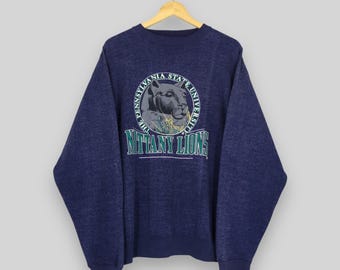 May include: Navy blue sweatshirt with a circular graphic featuring a lion and the text "The Pennsylvania State University" and "Nittany Lions" in white and green. The sweatshirt is hanging on a wooden hanger.