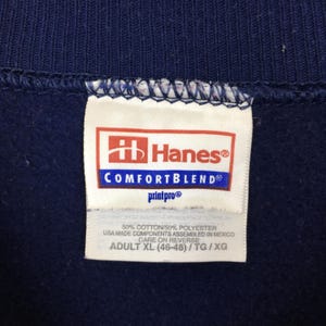 May include: A navy blue garment featuring a white Hanes ComfortBlend tag. The label displays the Hanes logo, 50% cotton and 50% polyester fabric composition, USA made components assembled in Mexico, and the size Adult XL (46-48).