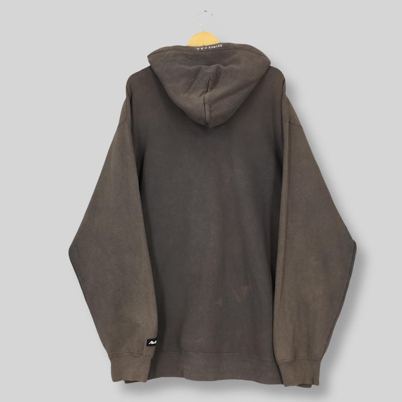 Puede incluir: Una sudadera con capucha marr&oacute;n con capucha con cord&oacute;n, mangas largas y un bolsillo de canguro. La sudadera con capucha tiene un aspecto descolorido y un peque&ntilde;o logotipo en la manga izquierda. La capucha tiene texto blanco.