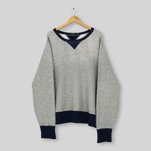 Puede incluir: Una sudadera gris con cuello en V, puños y dobladillo azul marino. La parte superior de manga larga está colgada de una percha de madera. El nombre de la marca es visible en el cuello.