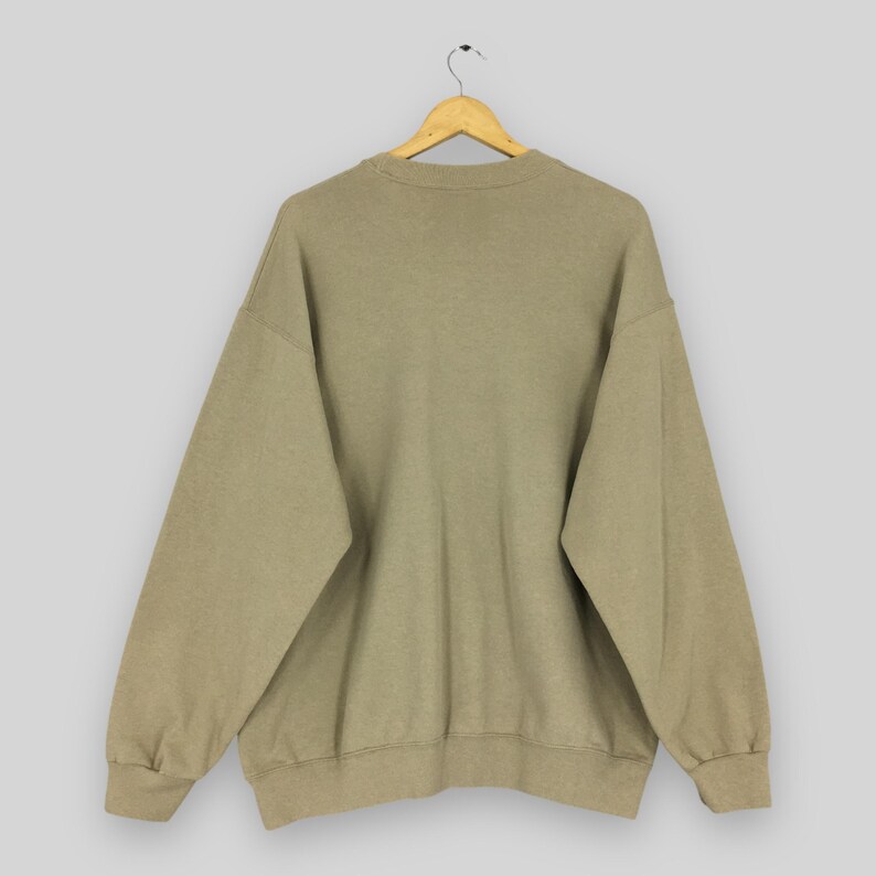 K&ouml;nnte beinhalten: Ein beigefarbenes Sweatshirt mit Rundhalsausschnitt und langen &Auml;rmeln, das an einem Holzb&uuml;gel h&auml;ngt. Das Sweatshirt hat eine lockere Passform und ein schlichtes Design, das sich f&uuml;r Freizeitkleidung eignet.
