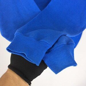 May include: Close-up of a royal blue sweatshirt sleeve. The ribbed cuff is a darker shade of blue. The sleeve is folded, revealing the soft fabric. The background is plain white.