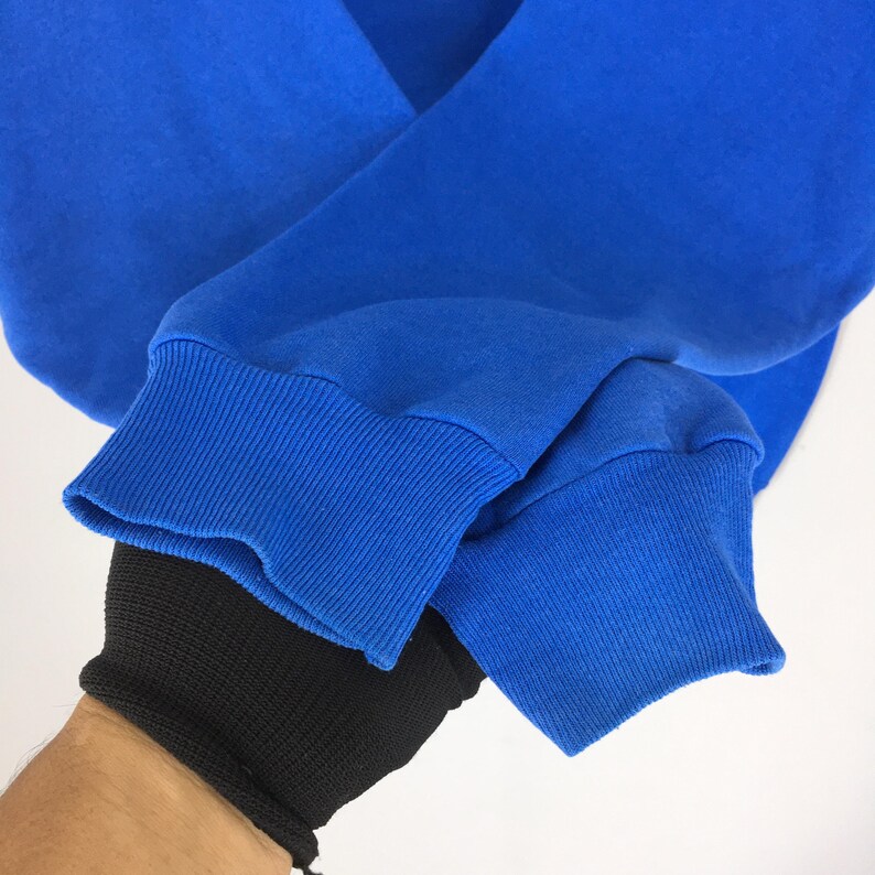 May include: Close-up of a royal blue sweatshirt sleeve. The ribbed cuff is a darker shade of blue. The sleeve is folded, revealing the soft fabric. The background is plain white.