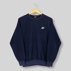 May include: Navy blue Nike sweatshirt with a small white Nike logo. The crew neck sweatshirt has long sleeves. The garment is suspended from a wooden hanger.