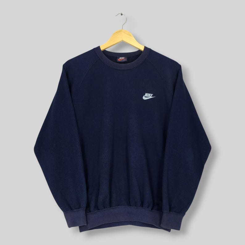 May include: Navy blue Nike sweatshirt with a small white Nike logo. The crew neck sweatshirt has long sleeves. The garment is suspended from a wooden hanger.