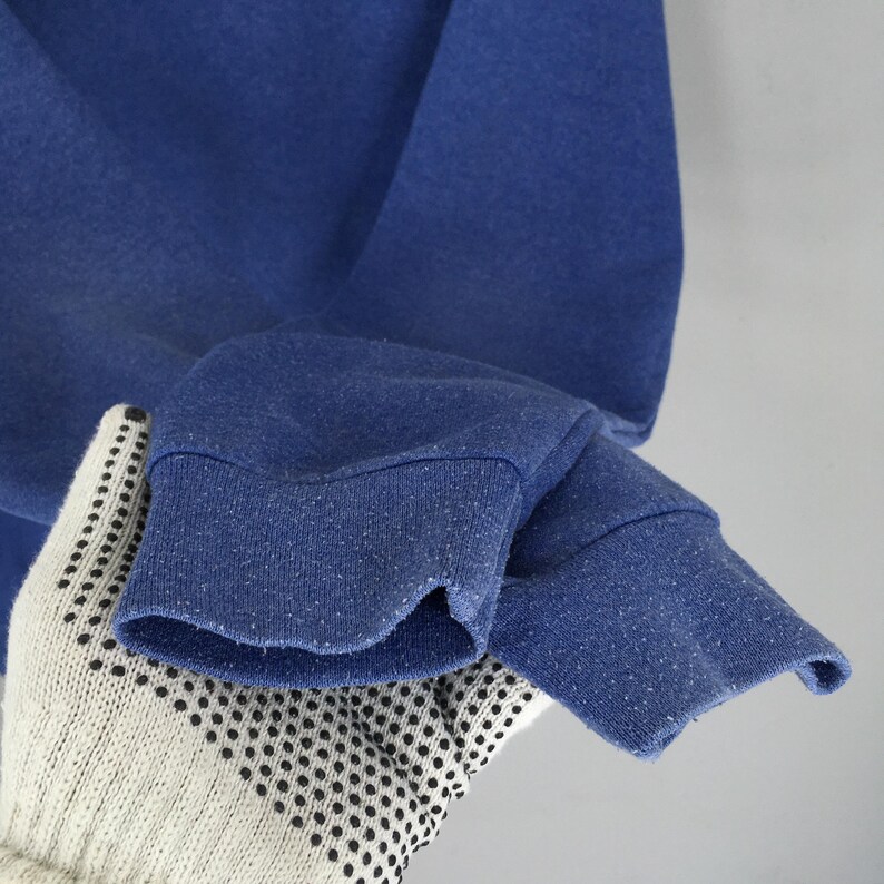May include: A solid blue long-sleeve sweatshirt featuring ribbed cuffs at the end of each sleeve. The fabric of the cuffs shows visible signs of pilling and wear, with a textured appearance across the blue cotton-blend material surface.