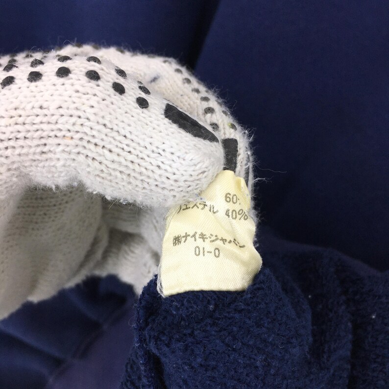 May include: Close-up of a navy blue garment with a tag held by a white glove with black dots. The tag has Japanese text and reads "60%" and "40%."