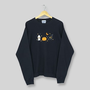 May include: Black crew neck sweatshirt with a Halloween embroidery. The design includes a ghost, a pumpkin, a black cat, a crescent moon, and stars. The sweatshirt has long sleeves and ribbed detailing at the neck, cuffs, and hem.