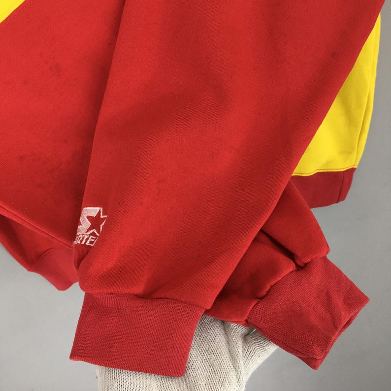 May include: Red and yellow vintage sweatshirt with a Starter logo on the sleeve. The sweatshirt has red cuffs and a red bottom hem. The sleeve is red with some discoloration. The back of the sweatshirt is yellow.