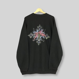 May include: Black sweatshirt with a colorful graphic on the back. The graphic is a cross-shaped design with pink, purple, and yellow accents. The sweatshirt is hanging on a wooden hanger.